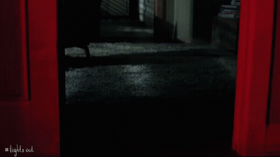 A Person Is Standing In A Dark Room With A Red Curtain . GIF