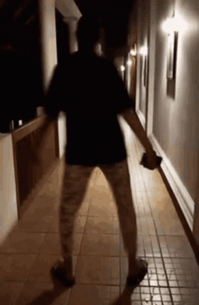 A Person Is Standing In A Hallway At Night Holding A Bottle . GIF
