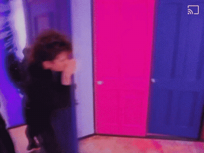 A Person Is Standing In A Room With Pink And Blue Doors And Covering Their Face . GIF
