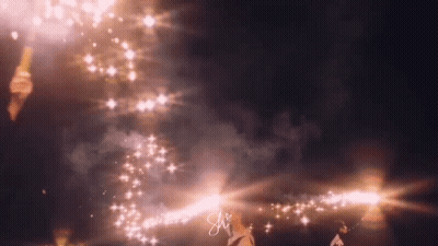 A Person Is Standing In Front Of A Fireworks Display With The Letter S On The Bottom Right Corner . GIF