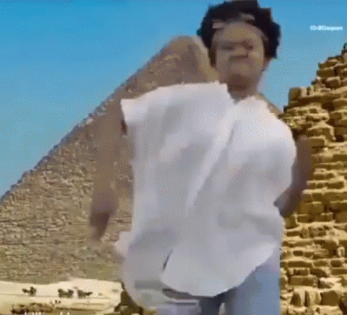 A Person Is Standing In Front Of A Pyramid Wearing A White Shirt . GIF