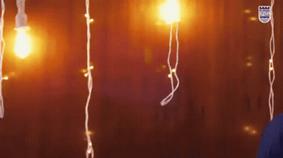 A Person Is Standing In Front Of A Wall With Christmas Lights Hanging From It GIF