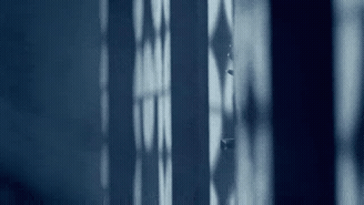 A Person Is Standing In Front Of A Window In A Dark Room And Looking Out . GIF