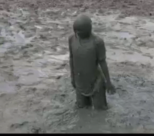 A Person Is Standing In The Mud In A Muddy Field . GIF