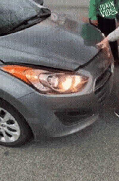 A Person Is Standing Next To A Gray Car With A Broken Hood And Headlight . GIF