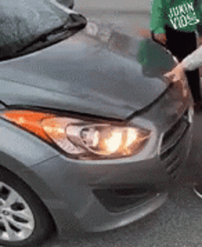 A Person Is Standing Next To A Gray Car With The Hood Up . GIF