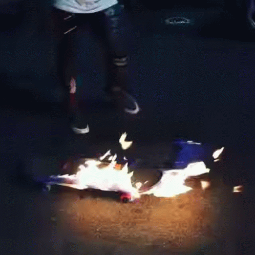 A Person Is Standing Next To A Skateboard That Is Burning . GIF