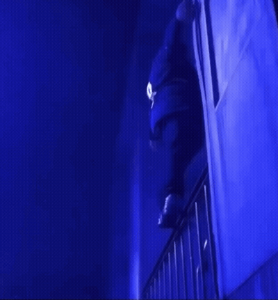 A Person Is Standing On A Railing In A Dark Room With Blue Lights GIF