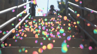 A Person Is Standing On A Set Of Stairs Surrounded By Colorful Soap Bubbles GIF