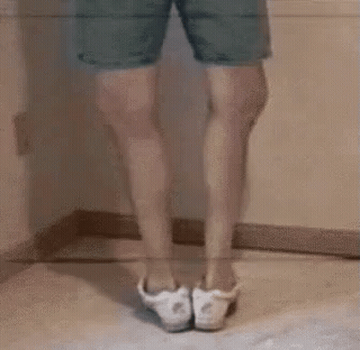 A Person Is Standing On A Wooden Floor With Their Legs Crossed And Wearing White Shoes . GIF