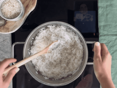 A Person Is Stirring A Pot Of Rice With A Wooden Spoon GIF