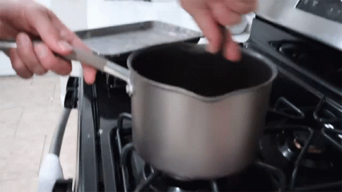 A Person Is Stirring A Pot On A Stove With A Spoon . GIF