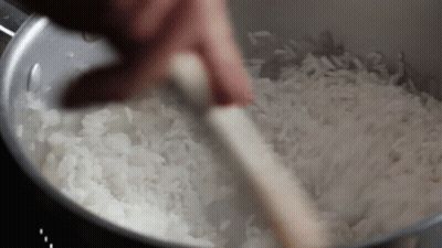 A Person Is Stirring Rice With A Wooden Spoon In A Pot . GIF