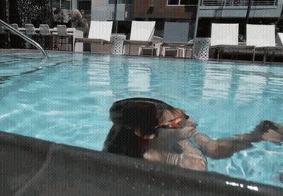 A Person Is Swimming In A Pool With A Reflection Of A Building In The Water GIF