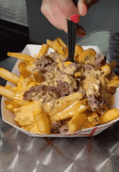 A Person Is Taking A Bite Of French Fries With Cheese GIF
