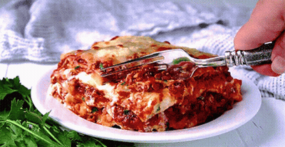 A Person Is Taking A Bite Of Lasagna With A Silver Fork GIF