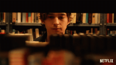 A Person Is Taking A Book Out Of A Bookshelf With A Netflix Logo In The Corner GIF