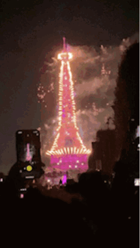 A Person Is Taking A Picture Of A Tower Lit Up At Night GIF