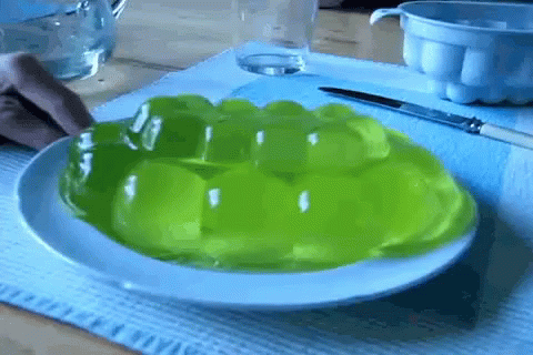 A Person Is Taking A Piece Of Green Jelly From A White Plate GIF