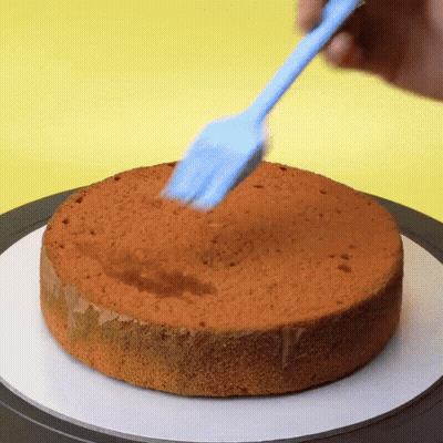 A Person Is Using A Blue Spatula On A Cake GIF
