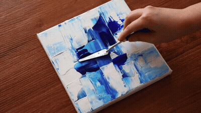 A Person Is Using A Palette Knife To Spread Blue Paint On A Canvas GIF