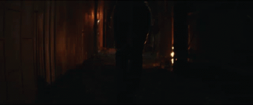 A Person Is Walking Down A Dark Alleyway With A Fire In The Background GIF