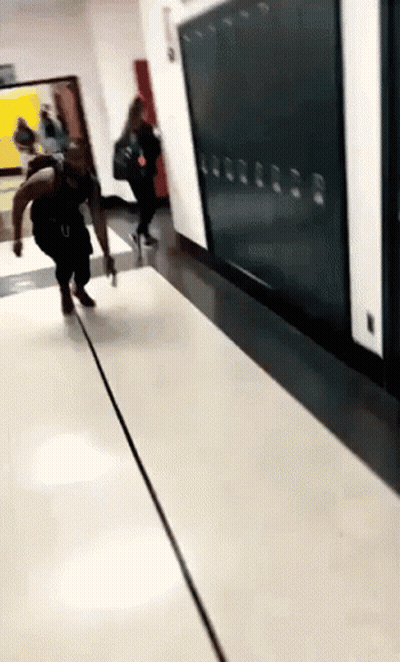A Person Is Walking Down A Hallway With Lockers On The Wall . GIF