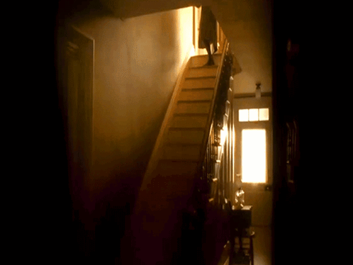 A Person Is Walking Down A Set Of Stairs In A Dark Room GIF