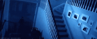 A Person Is Walking Down A Set Of Stairs In A Dark Room With Pictures On The Wall . GIF