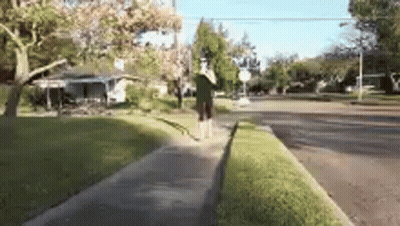 A Person Is Walking Down A Sidewalk In Front Of A House . GIF