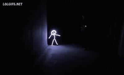 A Person Is Walking Through A Dark Room With A Stick Figure Drawn On The Wall . GIF