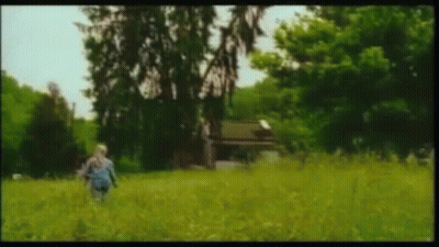 A Person Is Walking Through A Grassy Field With Trees In The Background . GIF
