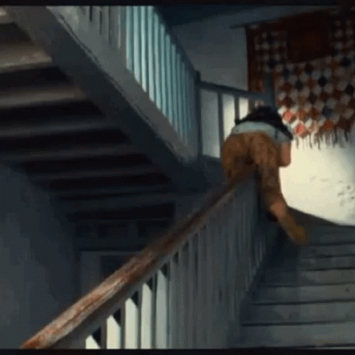 A Person Is Walking Up A Set Of Stairs With A Wooden Railing GIF