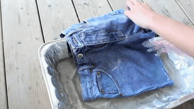 A Person Is Washing A Pair Of Jeans In A Tin Foil Tray GIF
