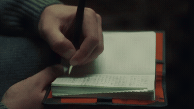 A Person Is Writing In A Notebook With A Pen On Top Of It GIF