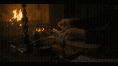A Person Is Writing In Front Of A Fireplace GIF