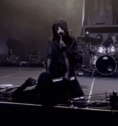 A Person Kneeling Down On A Stage With A Drum Set In The Background GIF