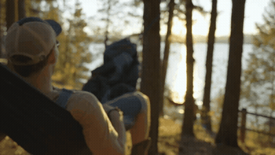 A Person Laying In A Hammock With A Backpack Looking At A Lake GIF