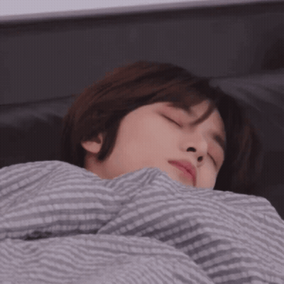A Person Laying In Bed With Their Eyes Closed And A Striped Blanket GIF
