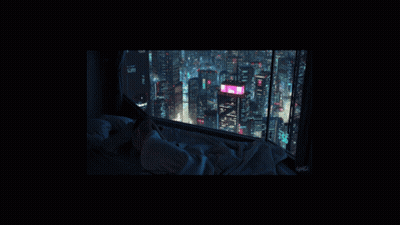 A Person Laying On A Bed Looking Out A Window At The City At Night GIF