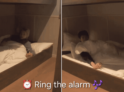 A Person Laying On A Bed Next To An Alarm Clock That Says " Ring The Alarm " On It GIF