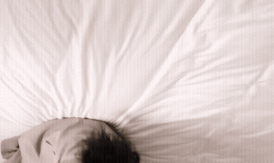 A Person Laying On A Bed With Their Head On A Pillow GIF