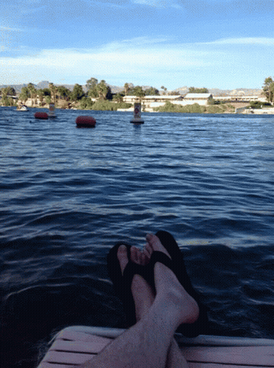 A Person Laying On A Dock With Their Feet In The Water With A Buoy In The Background GIF
