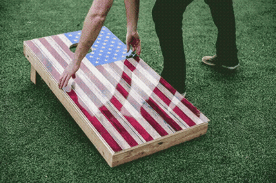 A Person Playing A Game Of Cornhole With An American Flag Design GIF