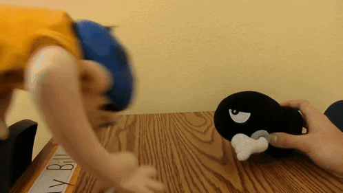 A Person Playing With A Stuffed Animal On A Wooden Table With A Sign That Says Billy Bill GIF