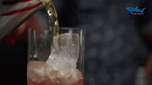A Person Pouring A Drink Into A Glass With Ice And A Shark Logo In The Background GIF