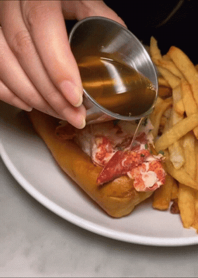 A Person Pouring Maple Syrup On A Lobster Roll GIF