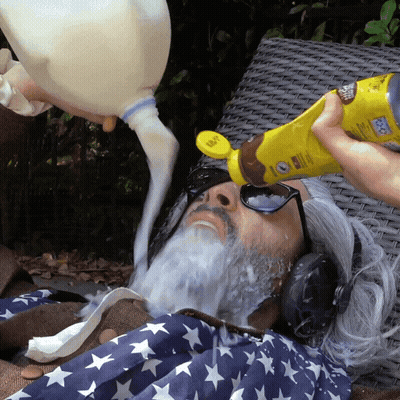 A Person Pouring Milk Into A Man 'S Face With A Bottle That Says Sunscreen On It GIF