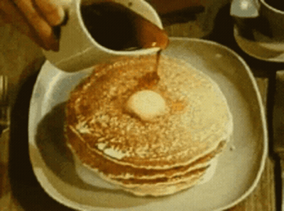 A Person Pouring Syrup On A Stack Of Pancakes With Butter GIF
