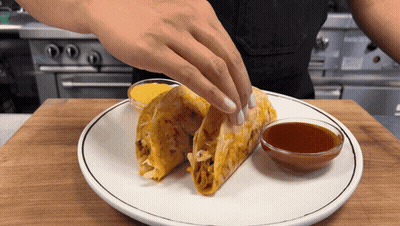 A Person Putting A Taco On A Plate With A Bowl Of Dipping Sauce GIF